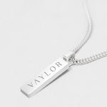 Silver necklace with a bar pendant engraved with 'VAYLOR' on a light gray background