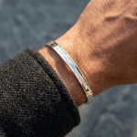 Close-up of a wrist wearing a silver and brown bracelet against a blurred background