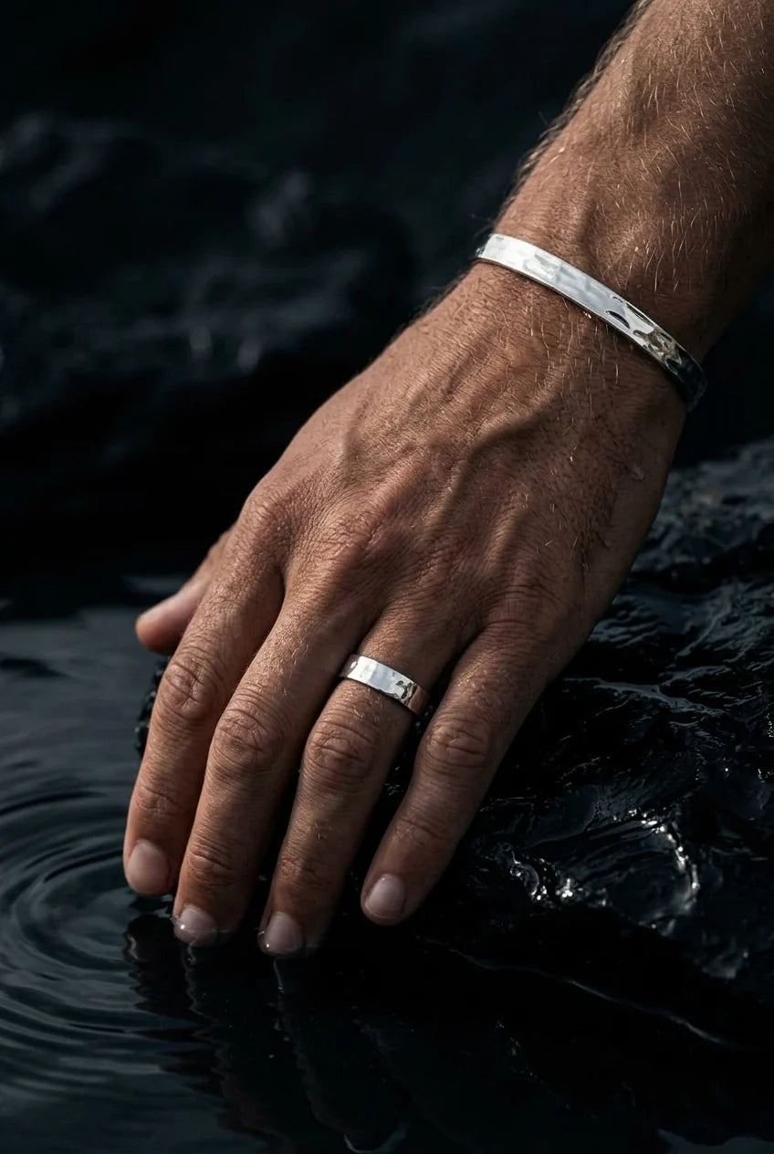 Hand with silver ring and bracelet resting on water
