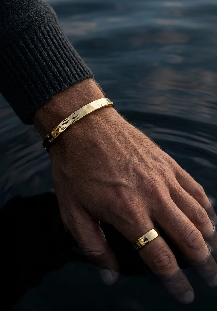 Hand wearing gold bracelets and a ring with water in the background