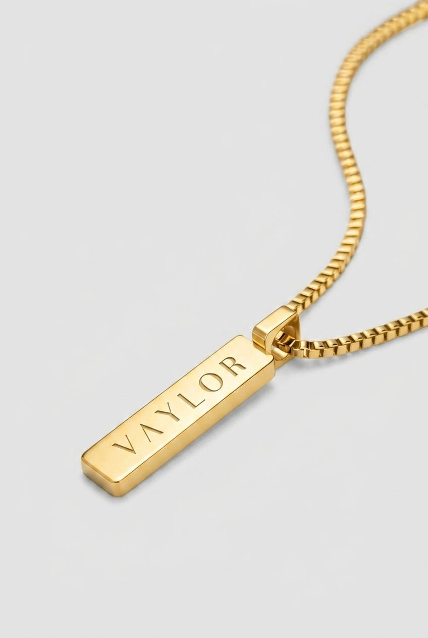 Gold necklace with a bar pendant on a light gray background
