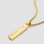 Gold necklace with a bar pendant on a light gray background
