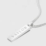 Silver necklace with a bar pendant engraved with 'VAYLOR' on a white background
