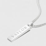 Silver necklace with a bar pendant engraved with 'VAYLOR' on a white background