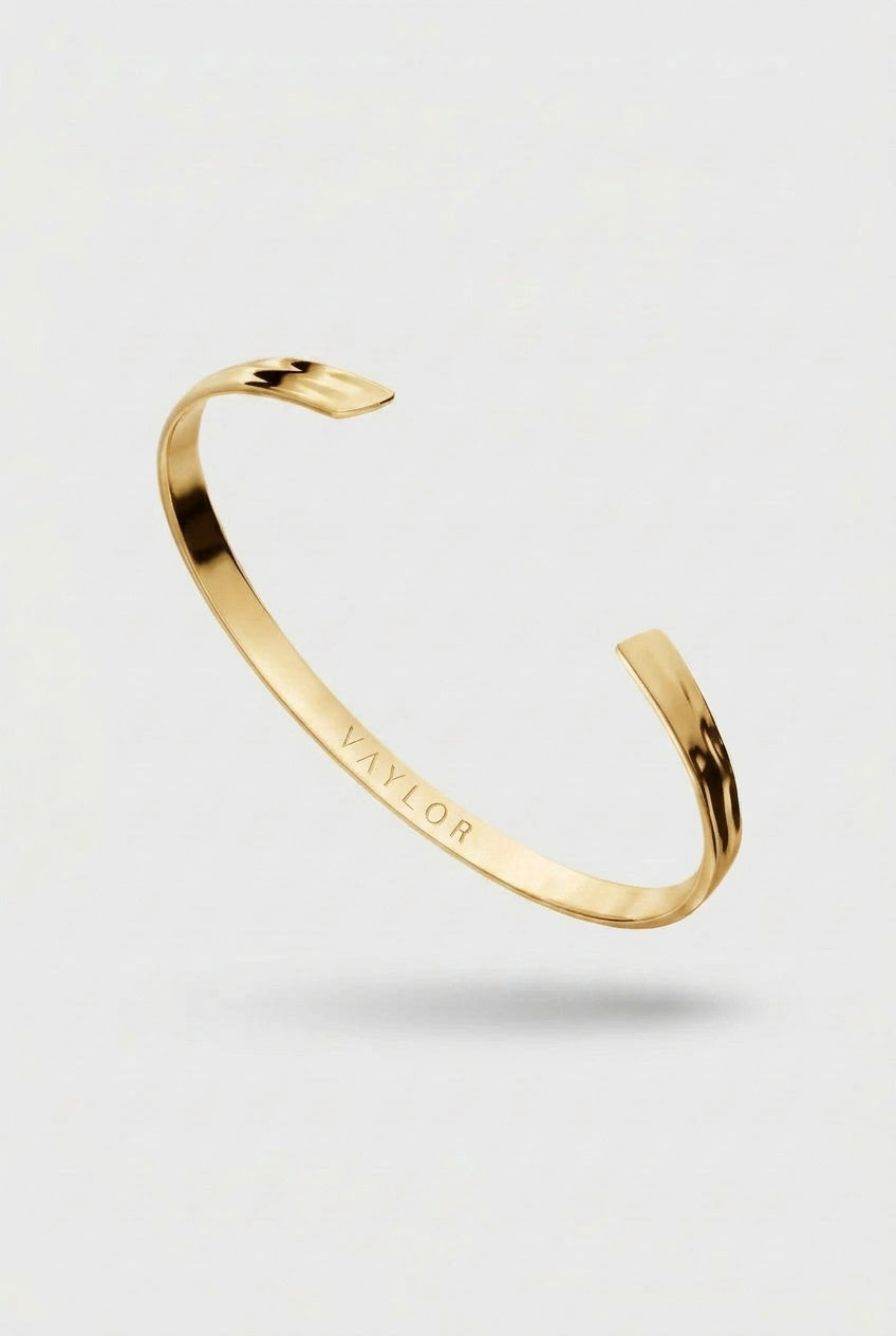 Gold bracelet with 'VAYLOR' engraving on a light gray background