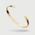 Gold bracelet with 'VAYLOR' engraving on a light gray background