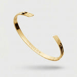 Gold bracelet with 'VAYLOR' engraving on a light gray background