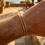 Close-up of a person's arm wearing gold bracelets with a scenic background.