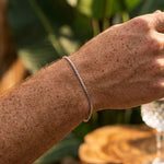 Close-up of a person's wrist wearing a silver bracelet with a blurred natural background