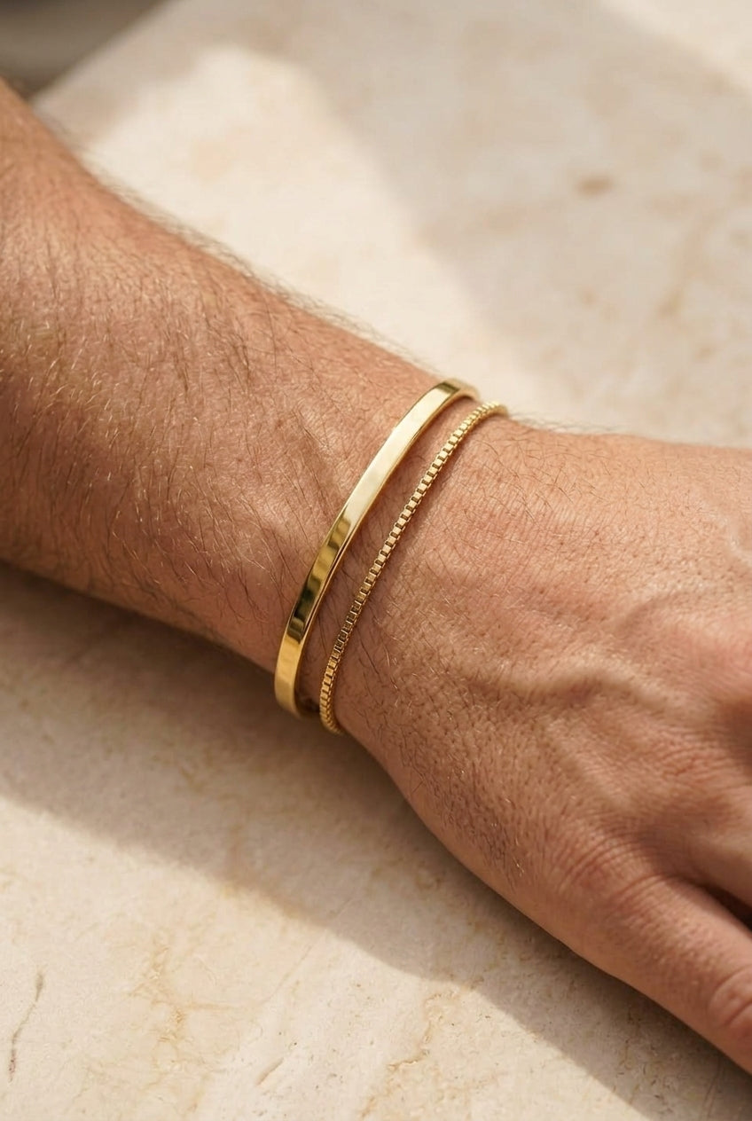 Gold bracelets on a wrist against a neutral background