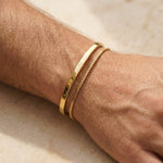 Gold bracelets on a wrist against a neutral background