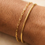 Gold bracelets on a person's wrist with a neutral background