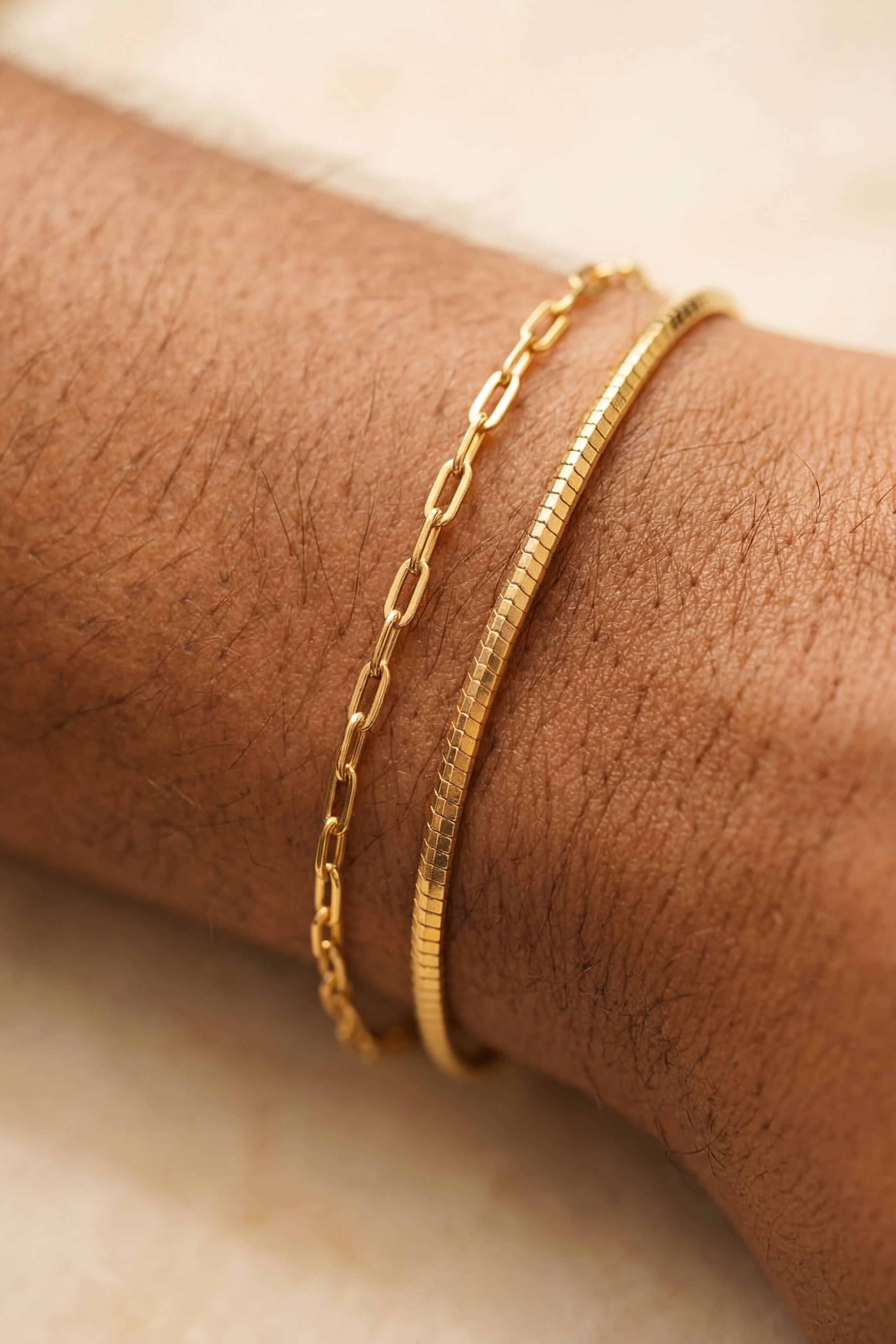 Gold bracelets on a person's wrist with a neutral background