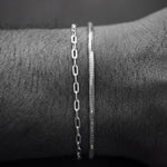 Two silver bracelets on a wrist against a dark background
