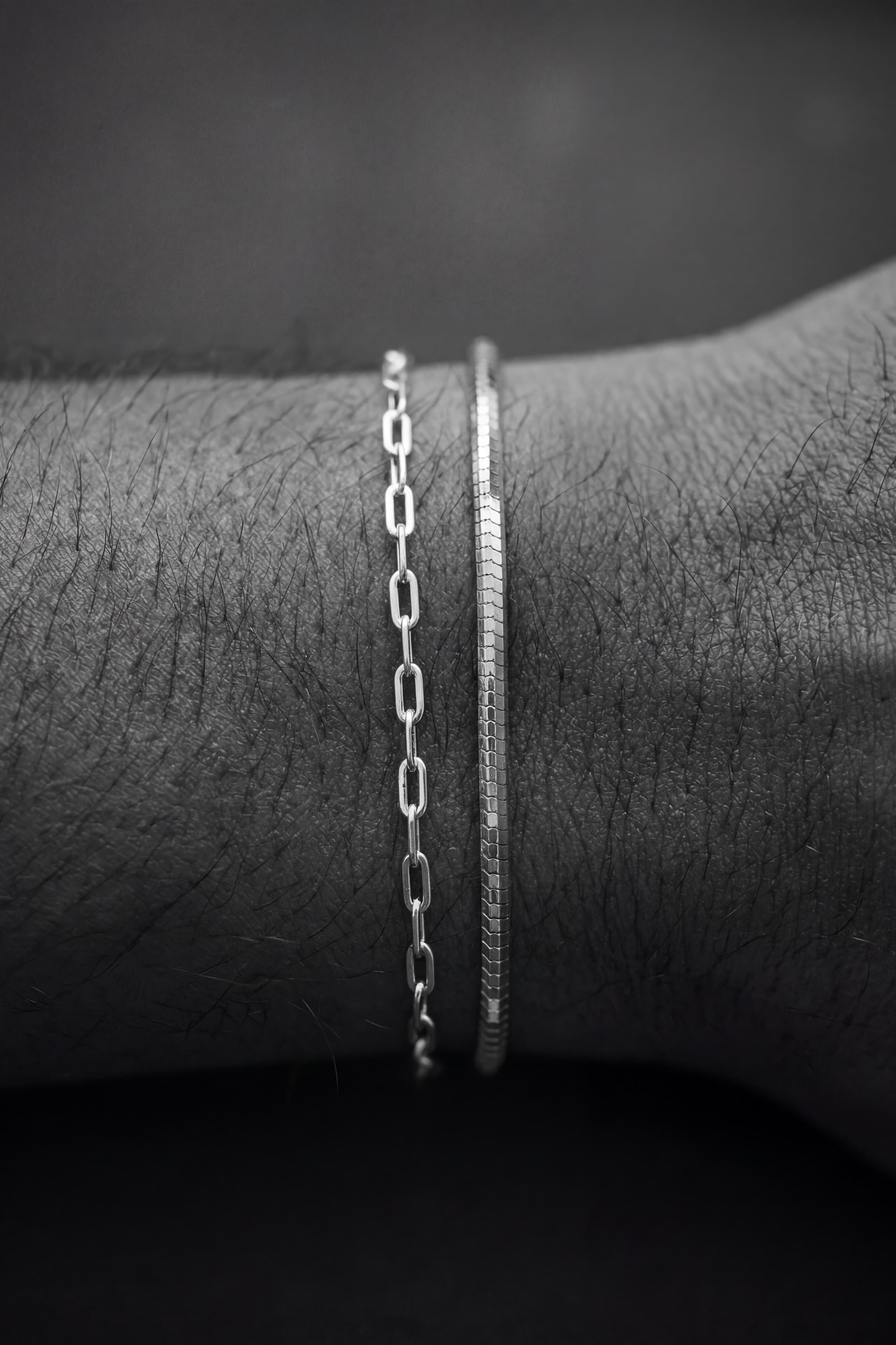 Two silver bracelets on a wrist against a dark background