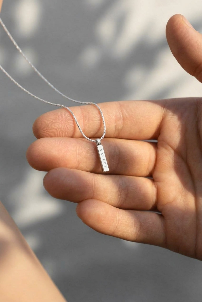 Hand holding a silver necklace with a pendant against a blurred background