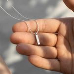 Hand holding a silver necklace with a pendant against a blurred background