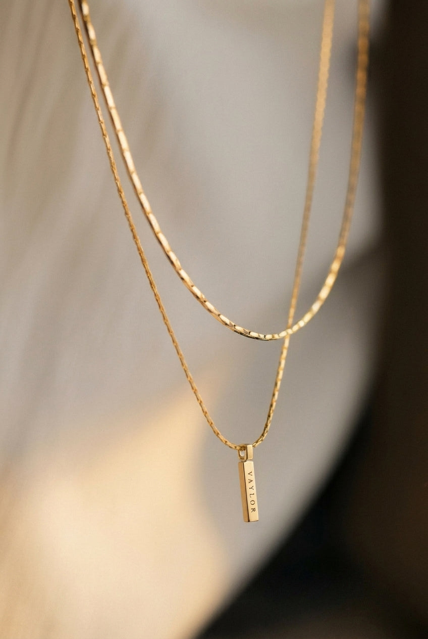 Two gold necklaces with a small pendant on a blurred background