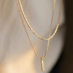 Two gold necklaces with a small pendant on a blurred background