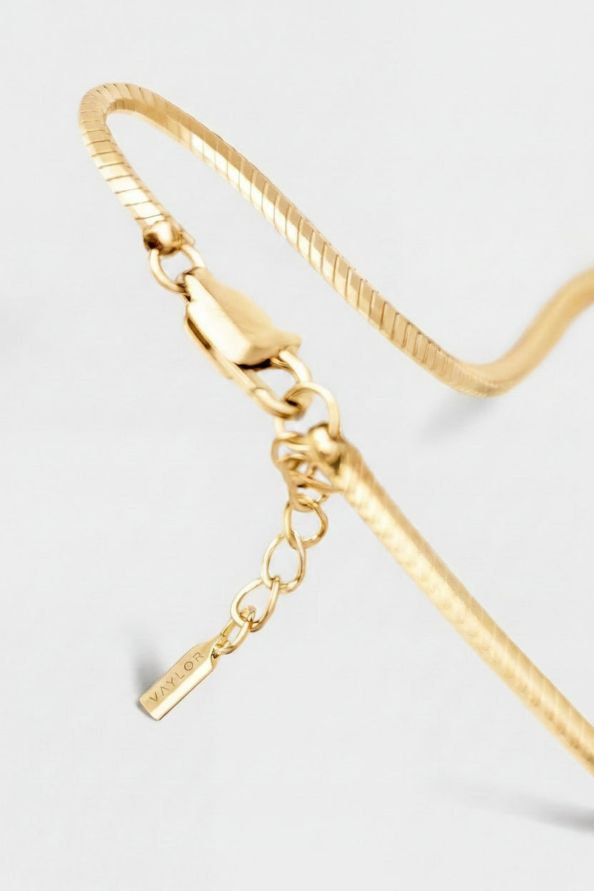 Gold bracelet with a small tag on a light gray background