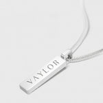 Silver necklace with a bar pendant engraved with 'VAYLOR' on a white background