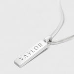 Silver necklace with a bar pendant engraved with 'VAYLOR' on a white background