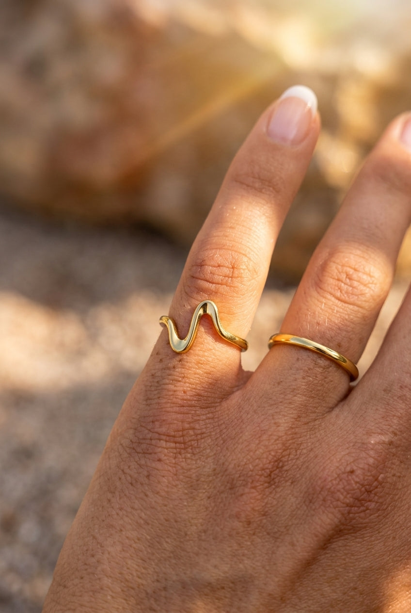 Hand wearing two gold rings with a blurred natural background