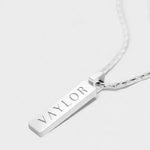Silver necklace with a bar pendant engraved with 'VAYLOR' on a white background