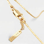 Gold bracelet with a tag on a light gray background