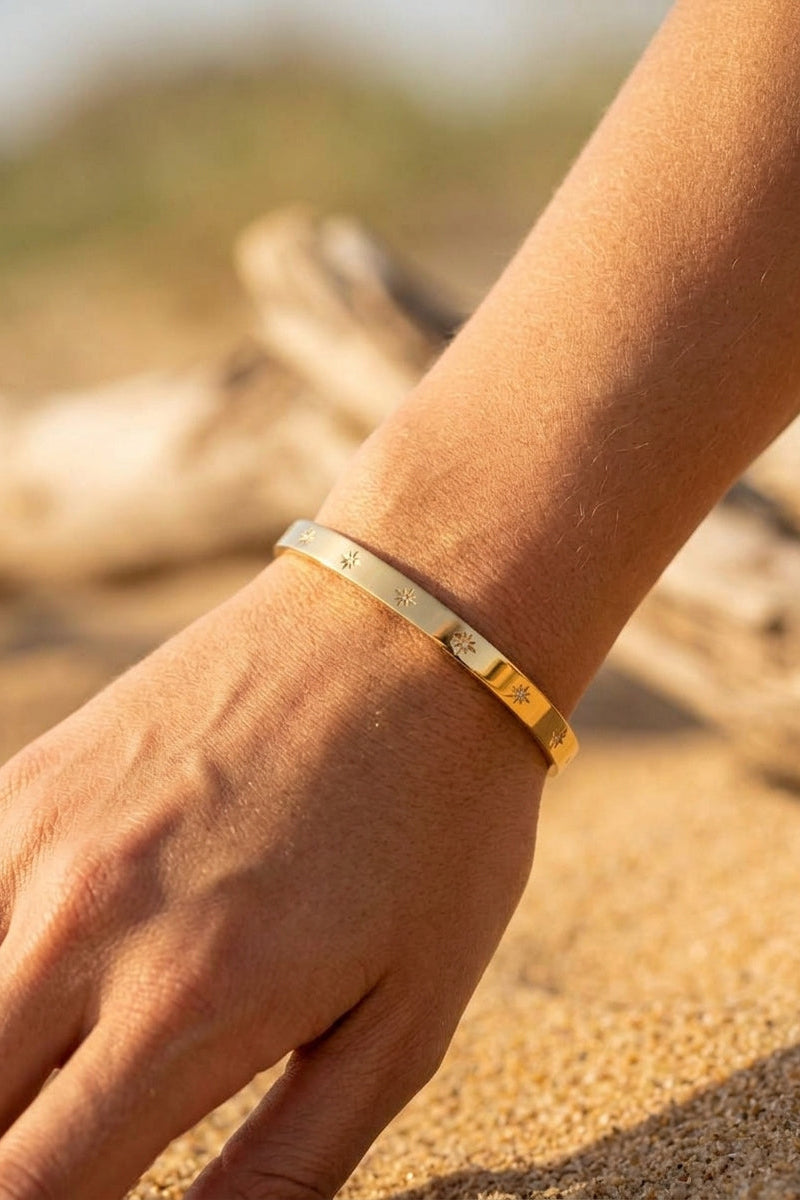 Gold bracelet on a wrist with a blurred natural background