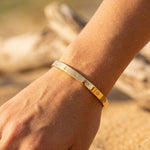 Gold bracelet on a wrist with a blurred natural background