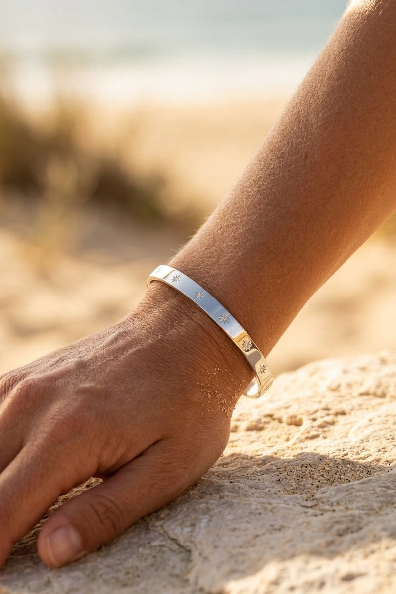 Hand wearing a silver bracelet on a sandy surface with a blurred natural background
