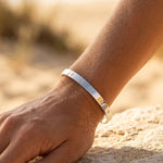 Hand wearing a silver bracelet on a sandy surface with a blurred natural background