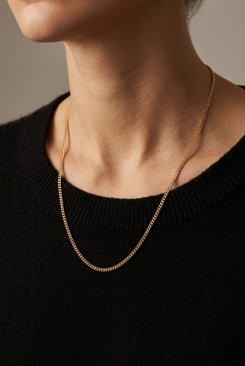 Gold chain necklace worn by a person against a neutral background