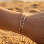 Silver chain bracelet on a person's wrist with a blurred beach background