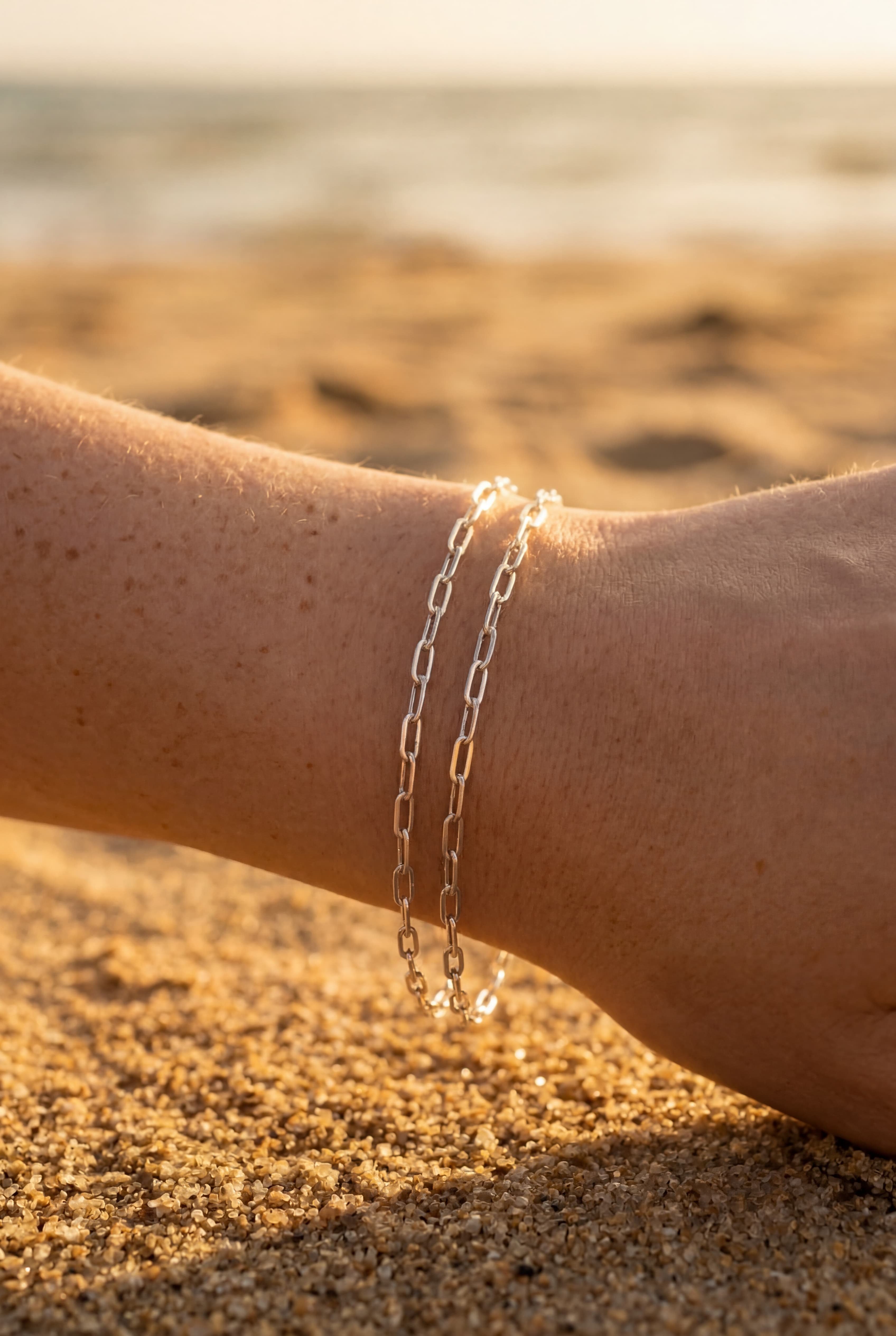 Silver chain bracelet on a person's wrist with a blurred beach background