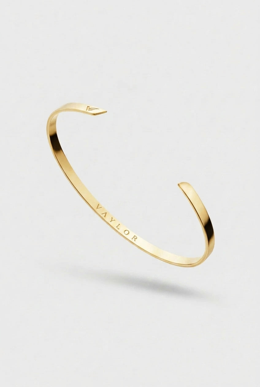 Gold bangle with 'Vaylor' engraving on a light gray background