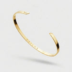 Gold bangle with 'Vaylor' engraving on a light gray background