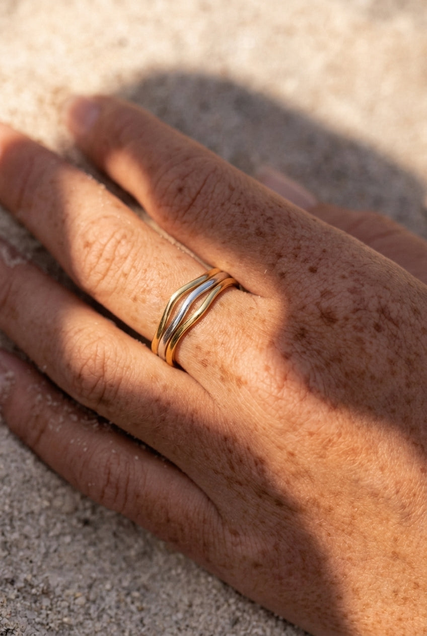Hand wearing a gold ring on a sandy surface