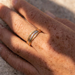 Hand wearing a gold ring on a sandy surface