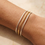 Close-up of a wrist wearing two gold bracelets on a light background
