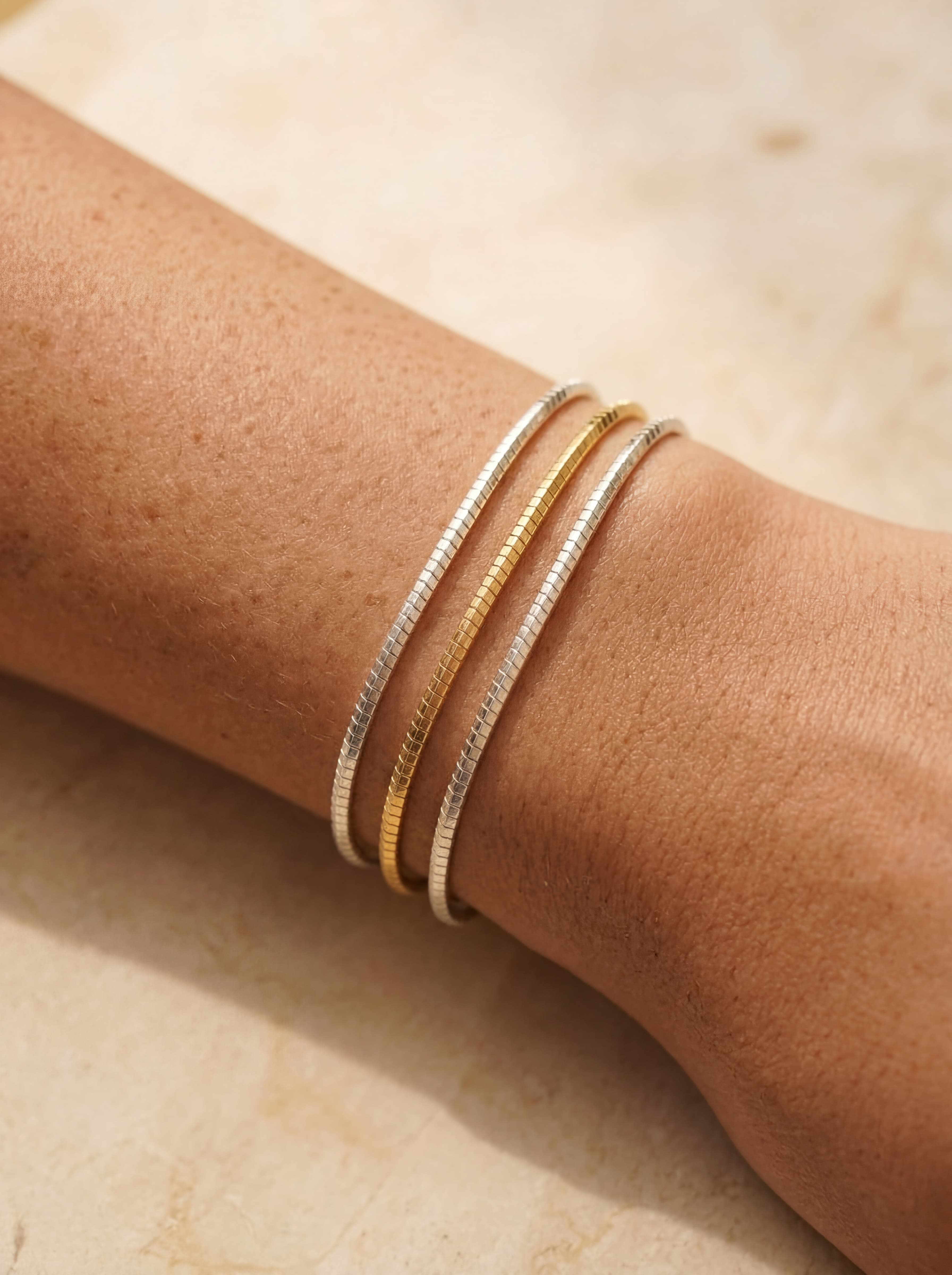 Close-up of a wrist wearing two gold bracelets on a light background