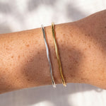 Gold and silver bangles on a person's wrist with a neutral background