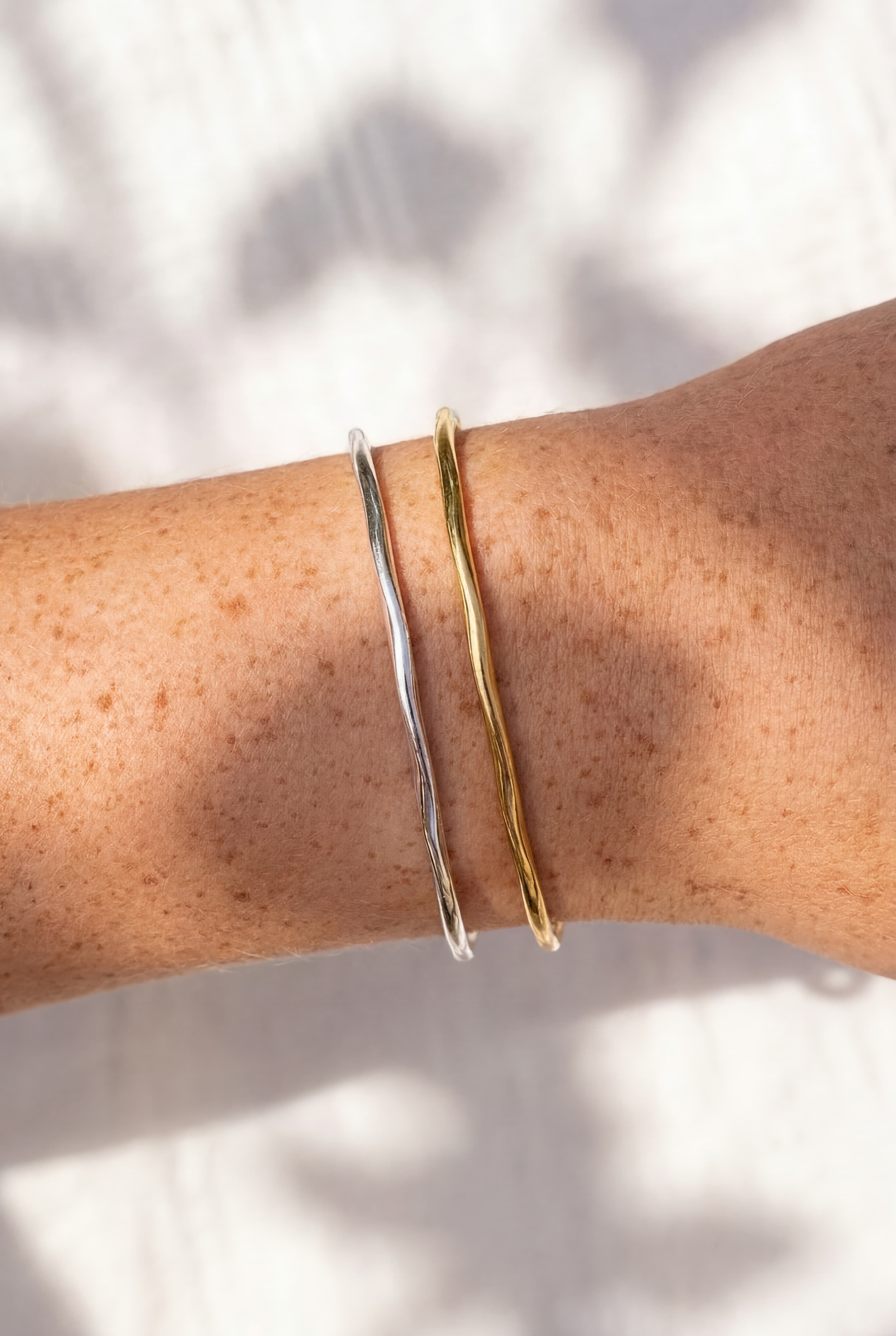 Gold and silver bangles on a person's wrist with a neutral background