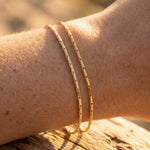 Gold bracelet on a wrist with a blurred natural background