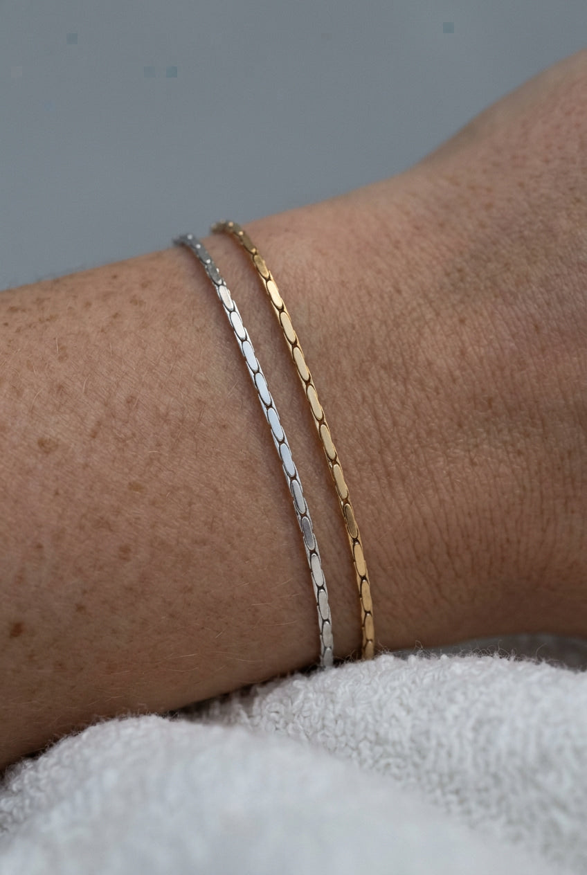 Two bracelets, one silver and one gold, on a wrist with a neutral background.