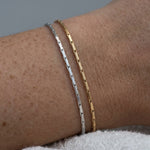 Two bracelets, one silver and one gold, on a wrist with a neutral background.