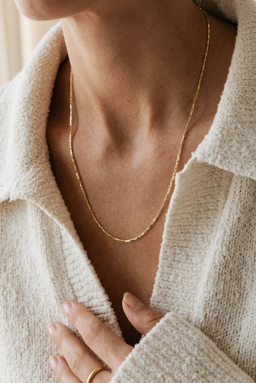 Close-up of a person wearing a gold necklace with a neutral background