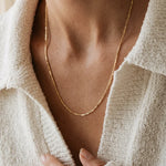 Close-up of a person wearing a gold necklace with a neutral background