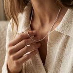 Close-up of a person wearing a silver necklace with a neutral background